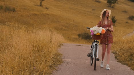 Mädchen-Im-Mittleren-Plan-Im-Kleid-Geht-Mit-Fahrrad-Und-Blumen-Auf-Dem-Feld